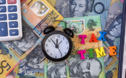 A small clock and block letters saying 'Tax Time' placed on Australian money.